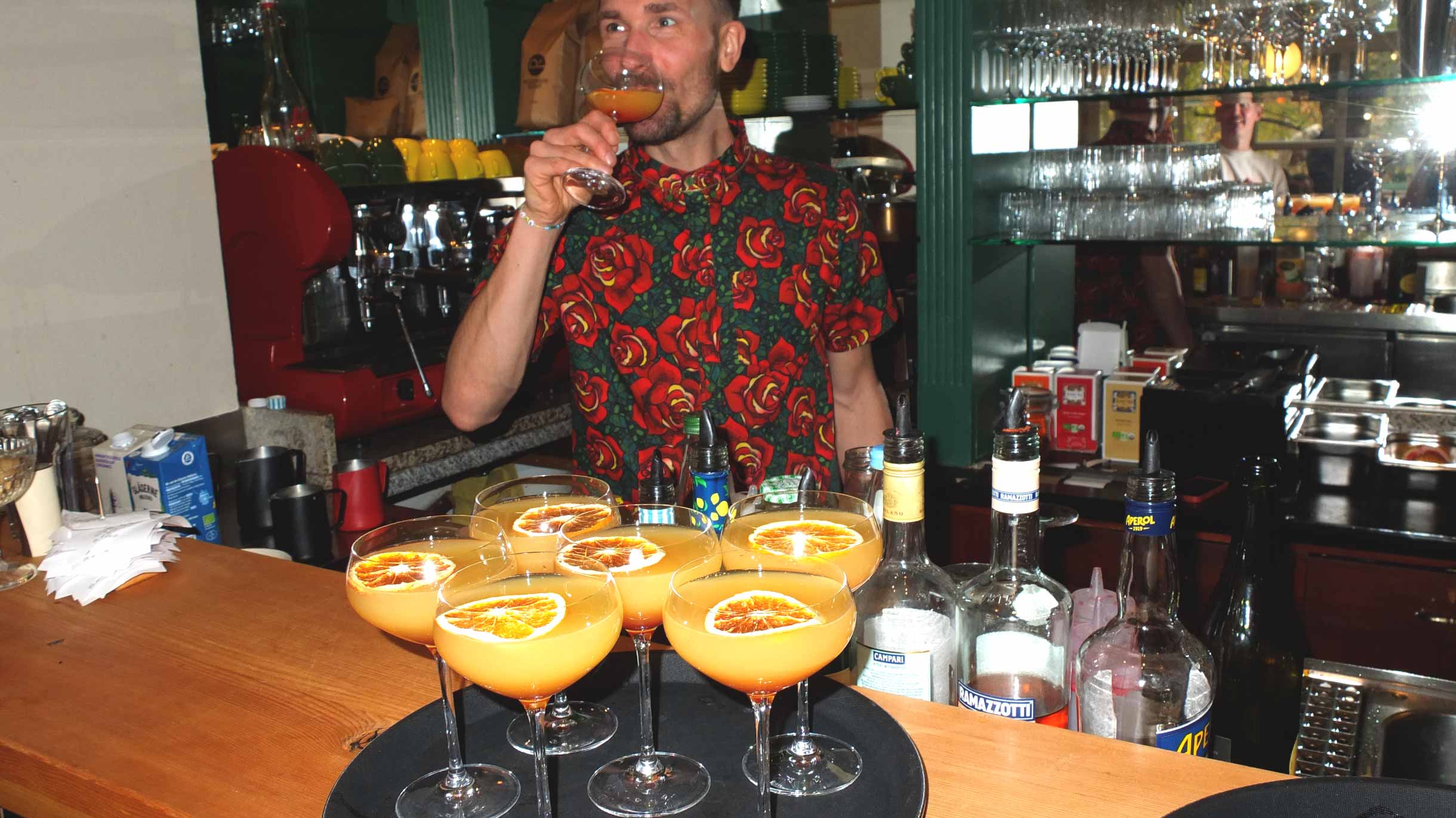 Max mixing Mimosas and testing it, standing behind the bar.